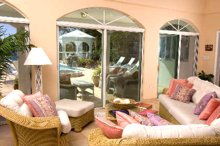 A cozy living room featuring wicker furniture and a view of a sparkling pool outside.