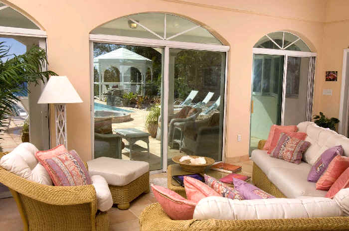 A cozy living room featuring wicker furniture and a view of a sparkling pool outside.