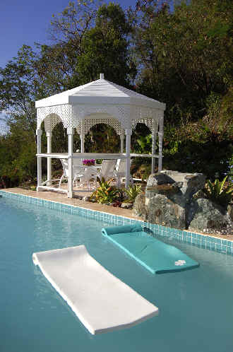A white gazebo stands elegantly in a garden, surrounded by lush greenery and colorful flowers.