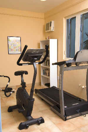 A home gym featuring various exercise equipment and a television mounted on the wall for workout guidance.