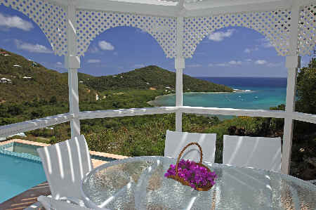 A gazebo with a table and chairs offers a scenic view of the ocean, surrounded by lush greenery.